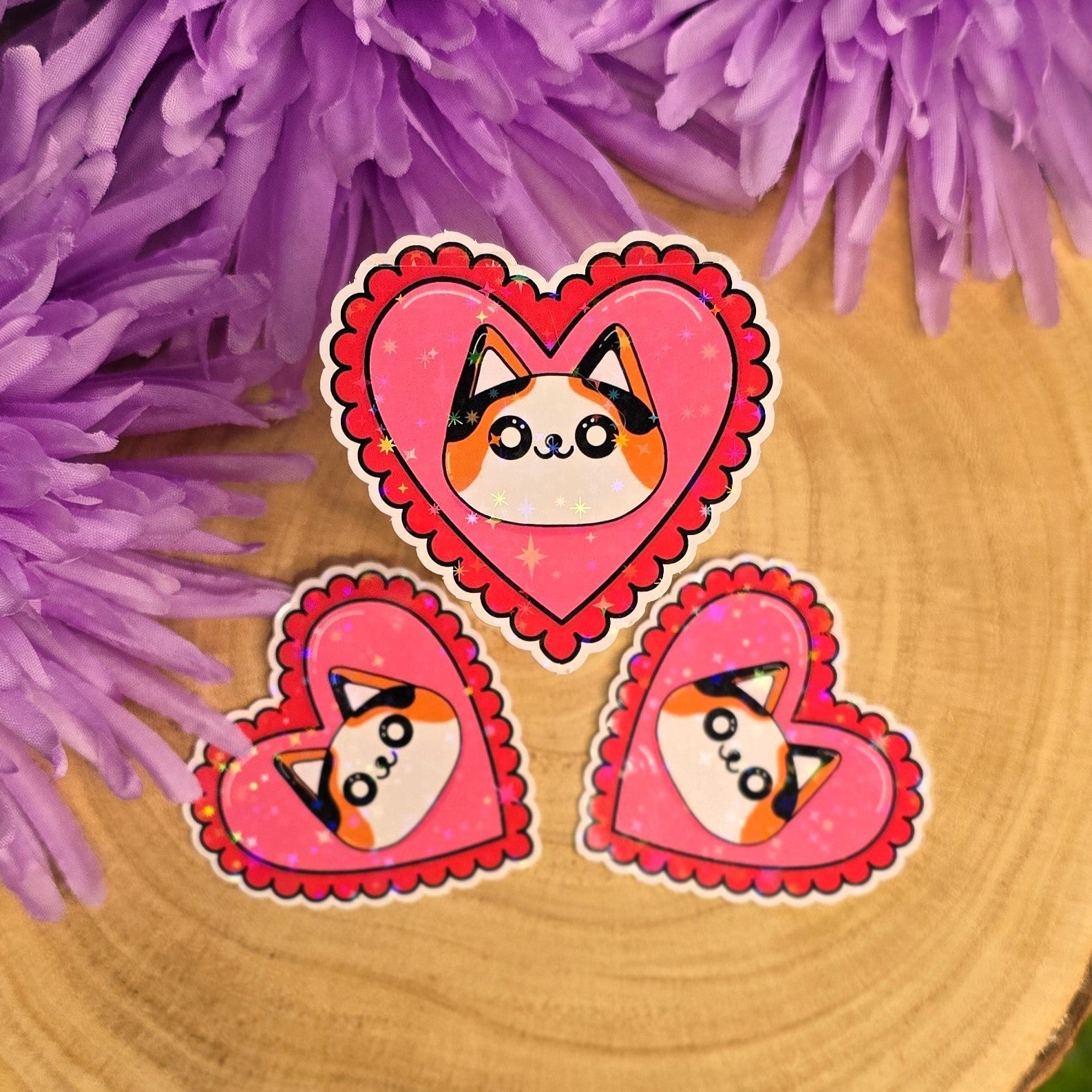Heart-shaped stickers with cat designs on a wooden surface with purple flowers in the background