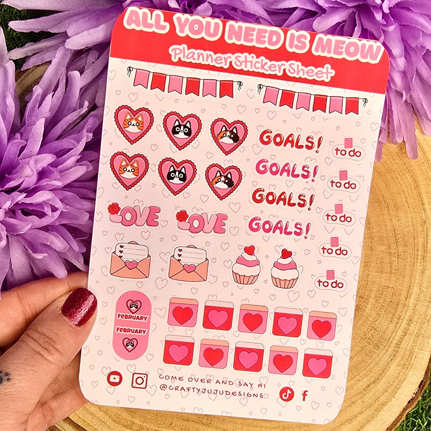 Sticker sheet with motivational designs held over purple flowers on a grassy background