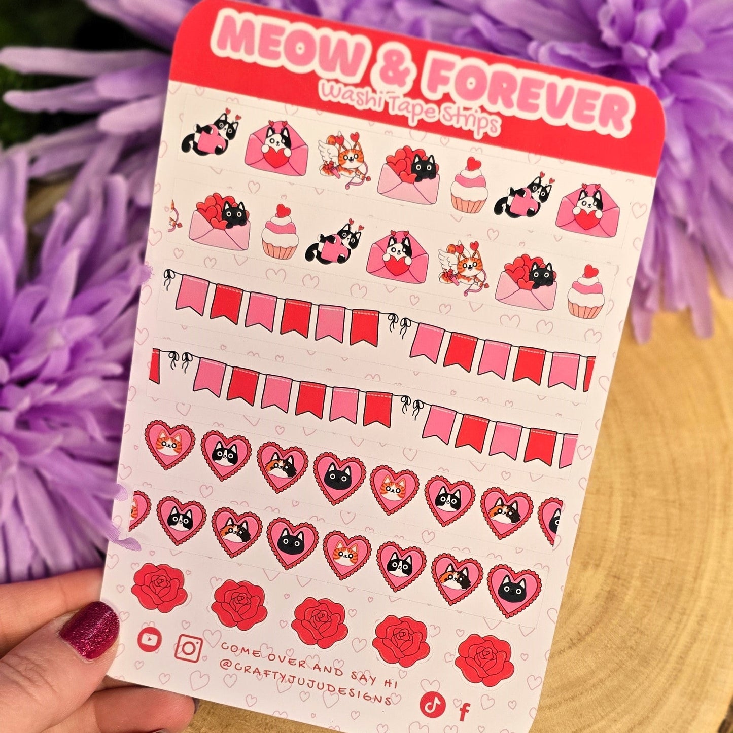 Sheet of stickers with cat-themed designs held over a wooden surface with purple flowers in the background