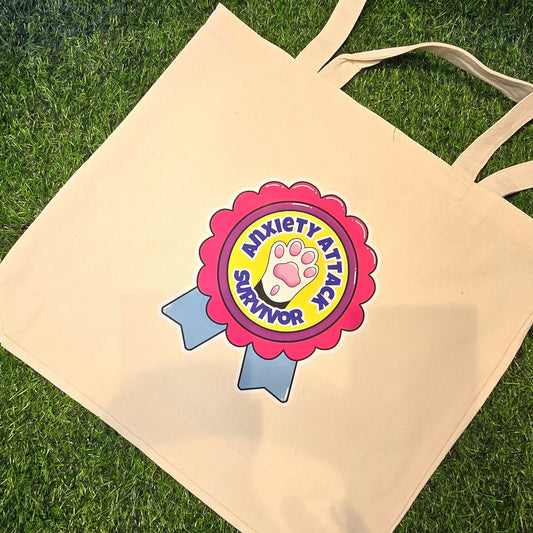 Beige tote bag with 'Anxiety Attack Survivor' design on grass