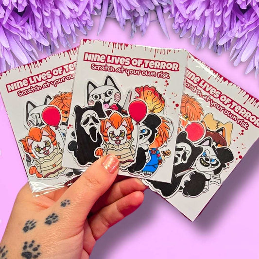 Three packaged sticker sheets featuring horror-themed cartoon characters from 'Nine Lives of Terror' are held by a hand against a pink background with purple tinsel.