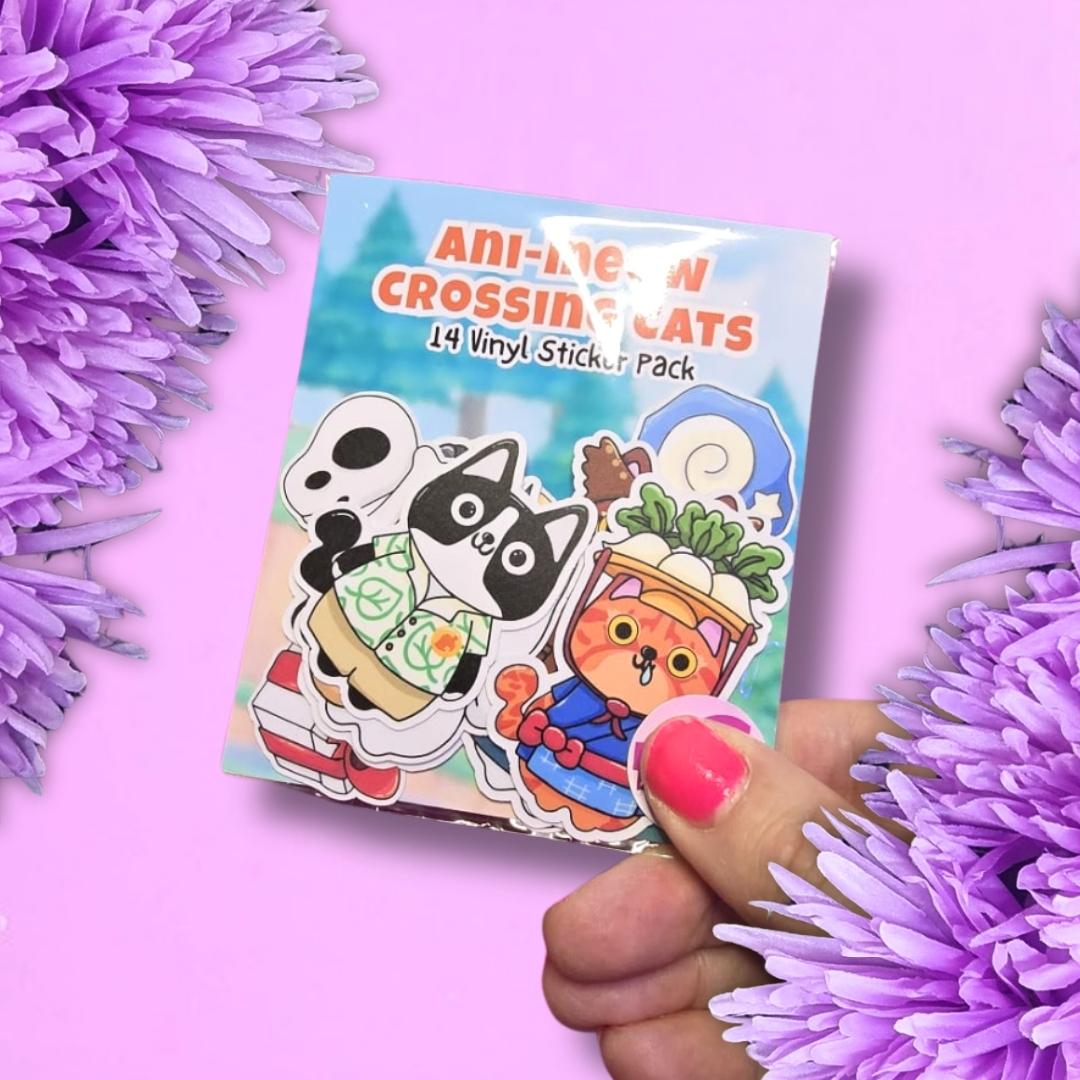 A hand with pink nail polish holds a sticker pack featuring cartoon cats, surrounded by purple flowers on a pink background. The sticker pack reads 'ANI-MESH CROSSING CATS 14 Vinyl Sticker Pack'.