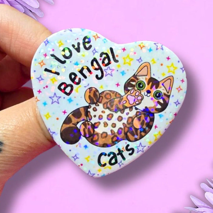 I love bengal cats holographic heart shaped pin badge with a brown spotty bengal cat showing you their belly. the background of the badge is white with multi vcoloured stars