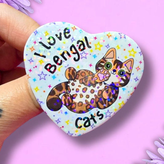 I love bengal cats holographic heart shaped pin badge with a brown spotty bengal cat showing you their belly. the background of the badge is white with multi vcoloured stars