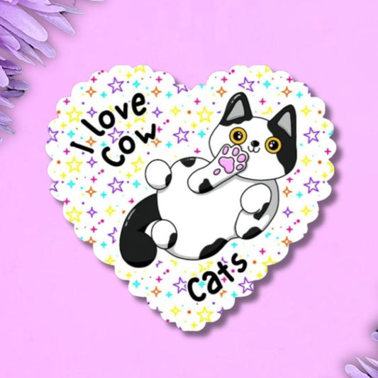 i love cow cats holographic heart shaped large vinyl sticker with scalloped edge detail. Back ground is white with multi coloured stars in different sizes. The cat is white with black markings