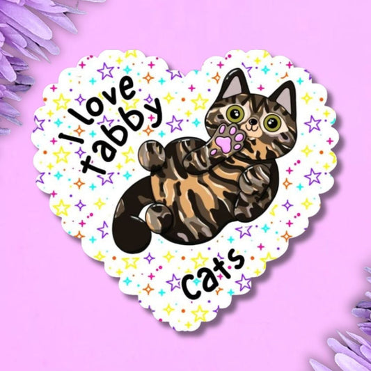 A heart-shaped sticker featuring an illustration of a tabby cat with the text 'I love tabby cats' and small colourful stars, shown on a purple background with purple flowers in the corners.