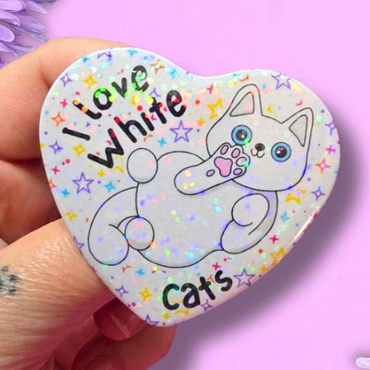 I love white cats holographic heart shaped pin badge with a white cat showing off its belly. The background of the badge is white with multi coloured stars