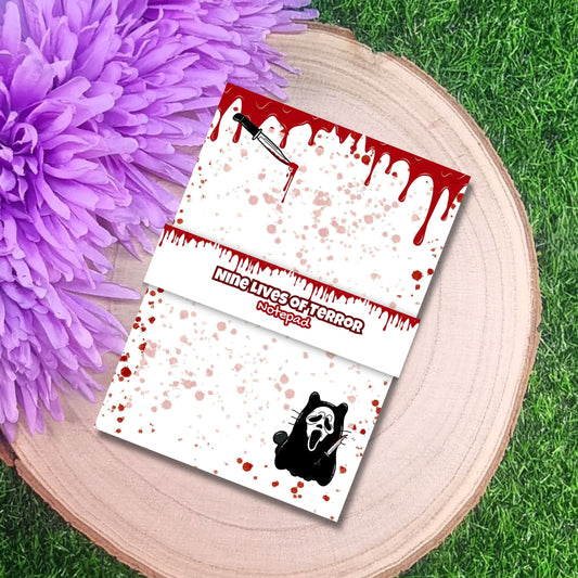 Notepad with horror-themed designs on a wooden surface with a purple flower.