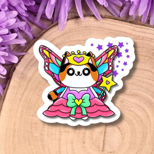 A die-cut sticker featuring a cute cartoon fairy cat in a pink dress with colorful wings, placed on a round wood slice surrounded by purple flowers.
