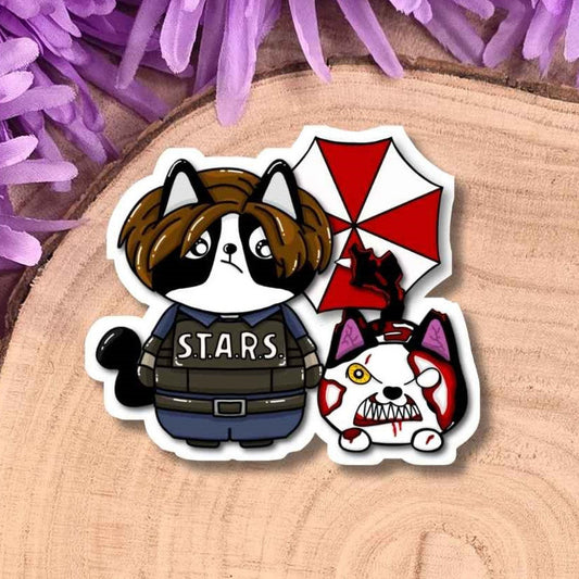 A die-cut sticker featuring two cartoon cats, one dressed as a police officer with the word 'STARS' on the chest and the other with a red-and-white umbrella, displayed on a wooden slice with purple flowers in the background.