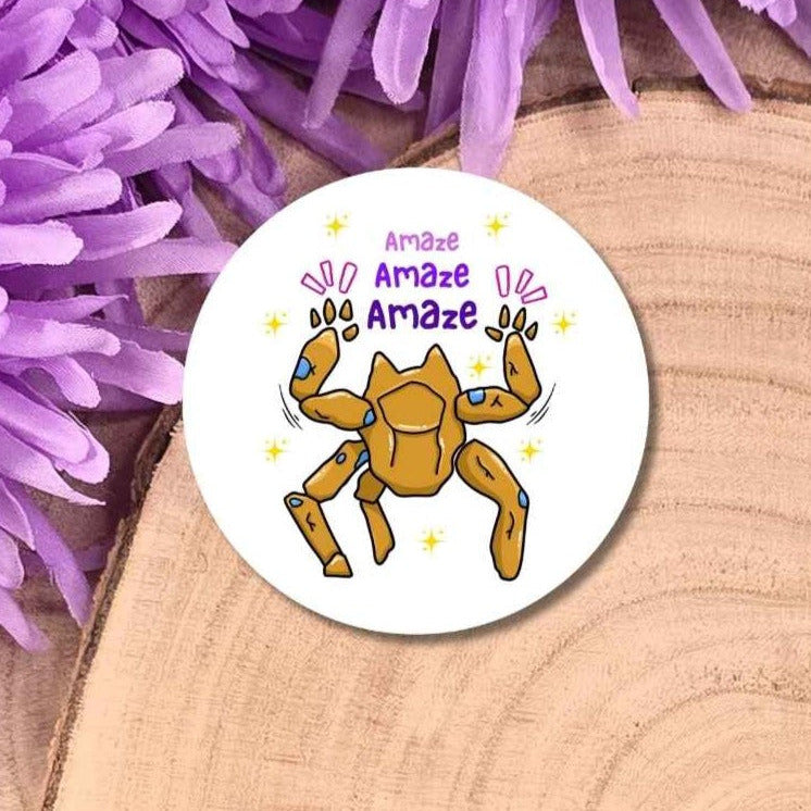 A round white sticker featuring a Rocky with purple text reading 'Amaze Amaze Amaze' and small yellow star accents, placed on a wood slice with purple flowers around it.
