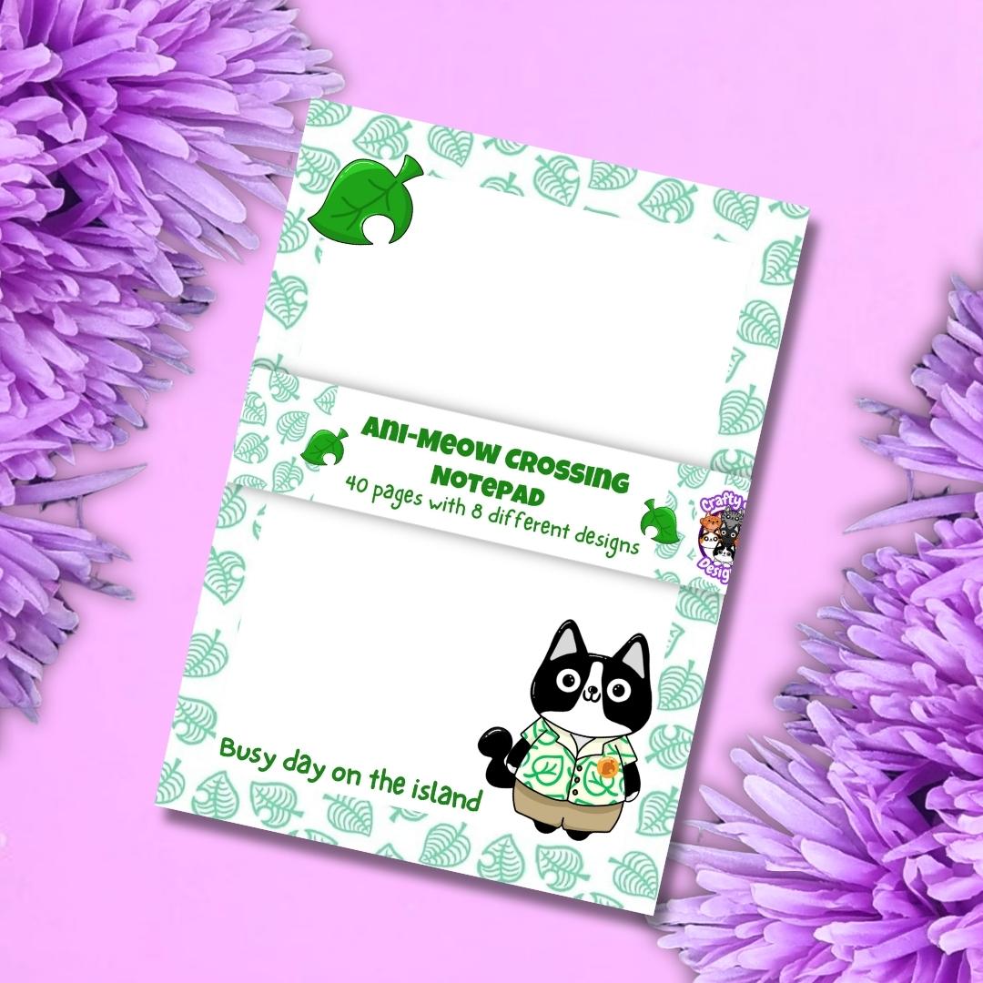 A notepad featuring the 'Ani-Mew Crossing' theme, styled flat-lay on a pink background with purple flowers. The notepad has a white base with a green leaf pattern border, a central white band with green text, and cartoon illustrations of a black cat in a green shirt and a green dog.