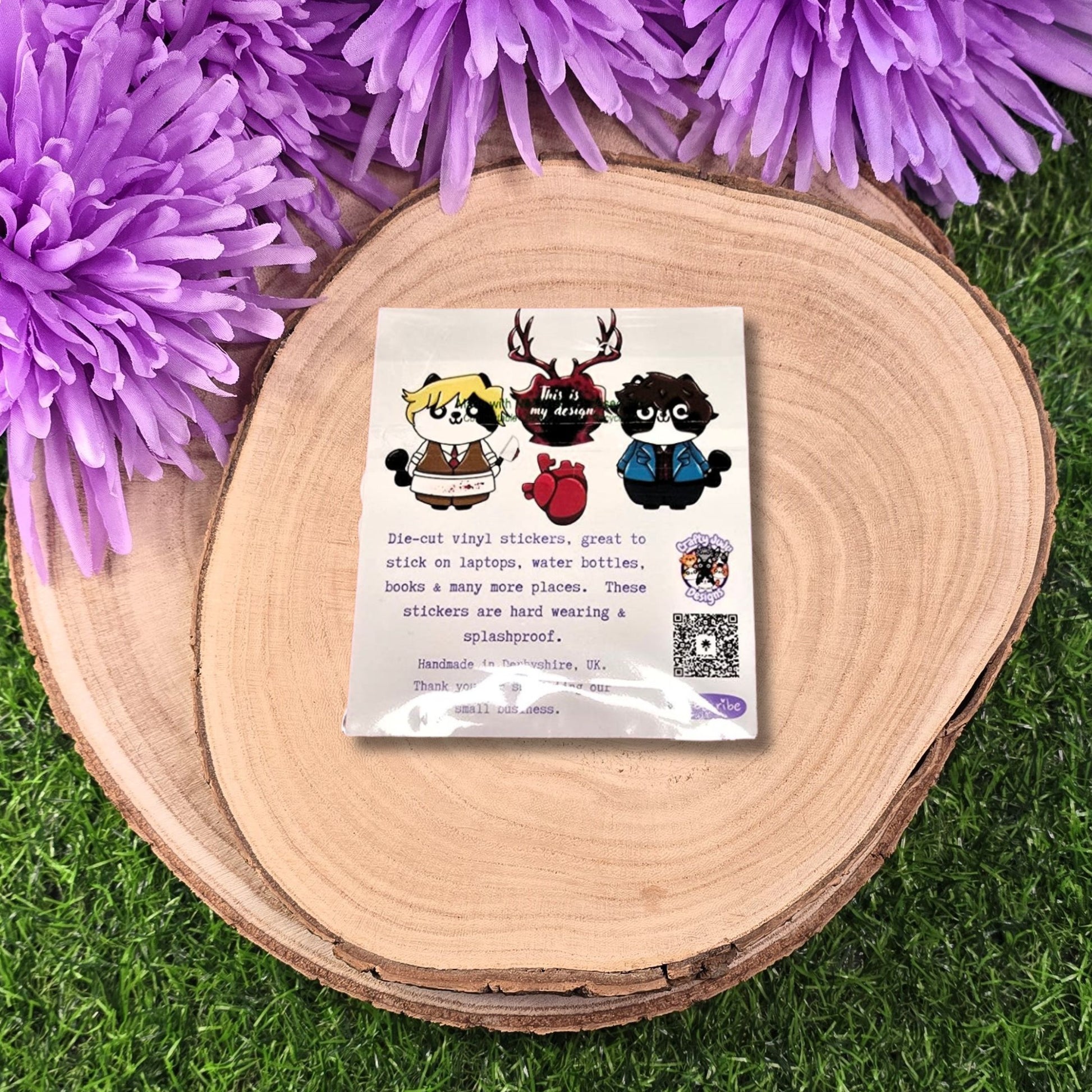 Pack of die-cut vinyl stickers on a wooden surface with purple flowers