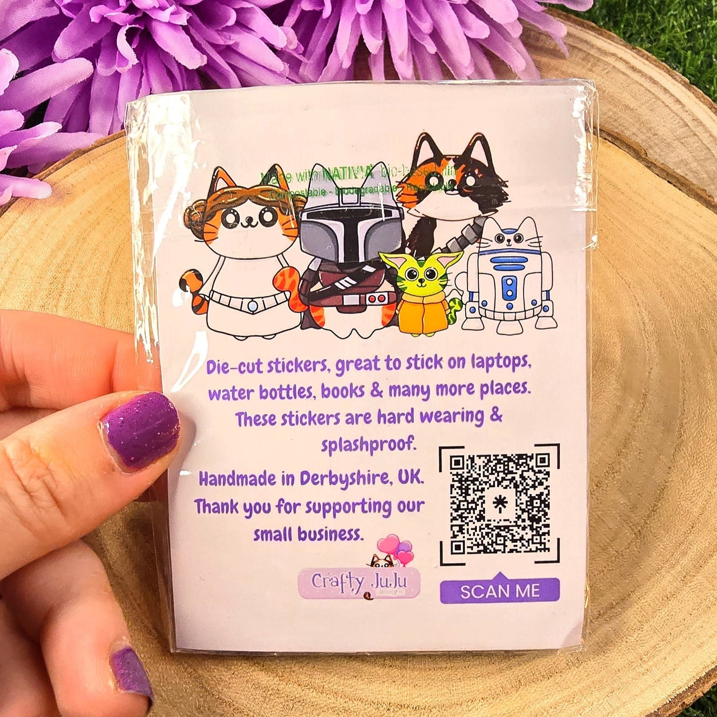 Hand holding a small product packaging with cartoon characters on a wooden surface with purple flowers in the background.