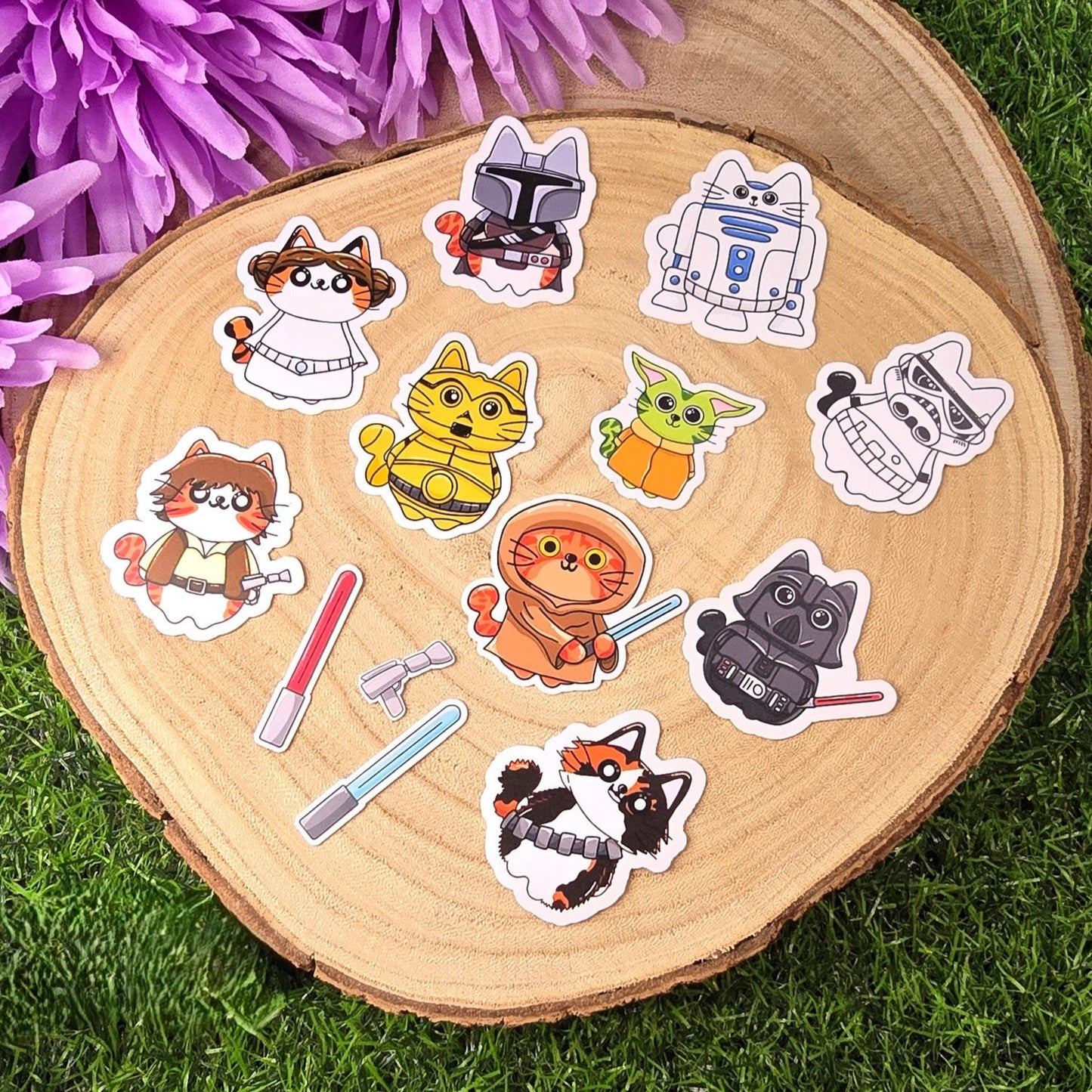 Set of cat-themed stickers on a wooden slice with grass and purple flowers in the background