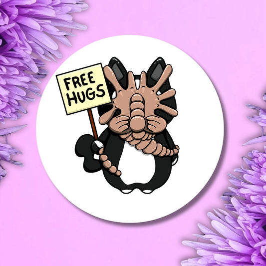 A round white badge featuring a cartoon black cat with its paws together holding a sign that reads 'FREE HUGS', set against a pink background with purple flowers in the corners.
