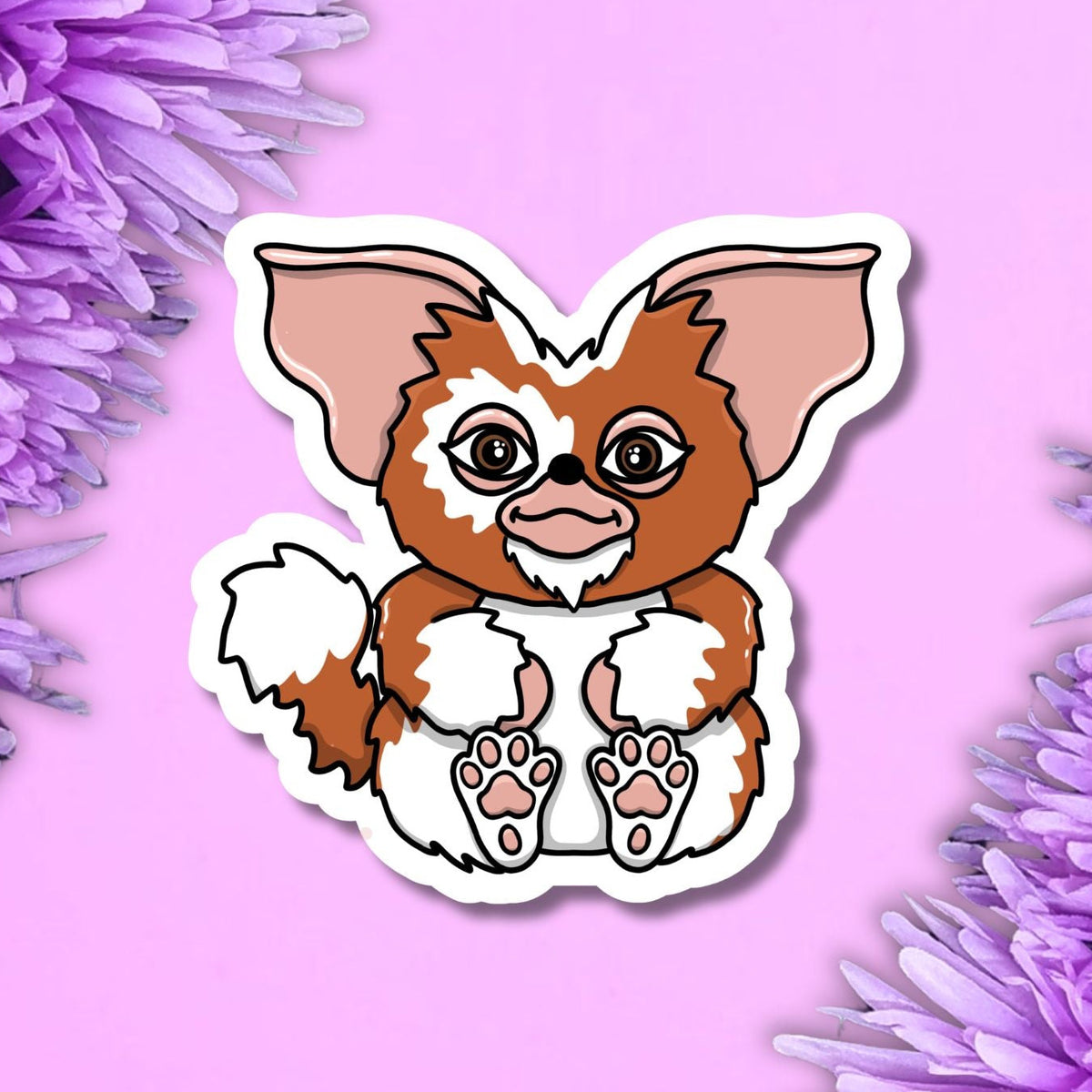 A die-cut sticker featuring an illustrated brown and white cartoon creature with large pink ears, shown on a pink background with purple flowers at the corners.