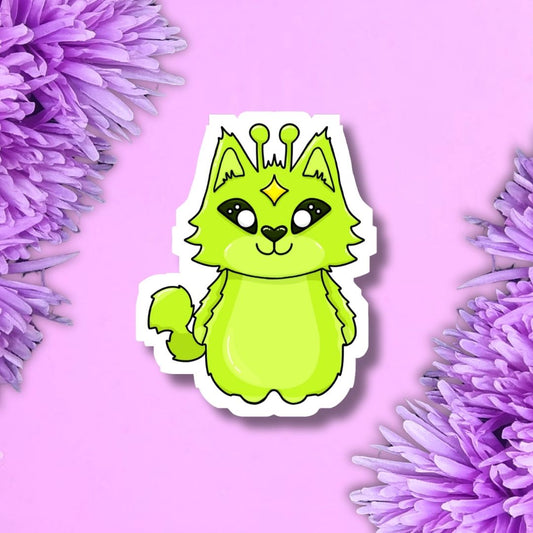 A die-cut sticker featuring a cute lime green cartoon cat with a small yellow diamond on its forehead and antennae, shown on a pink background with purple flowers in the corners.