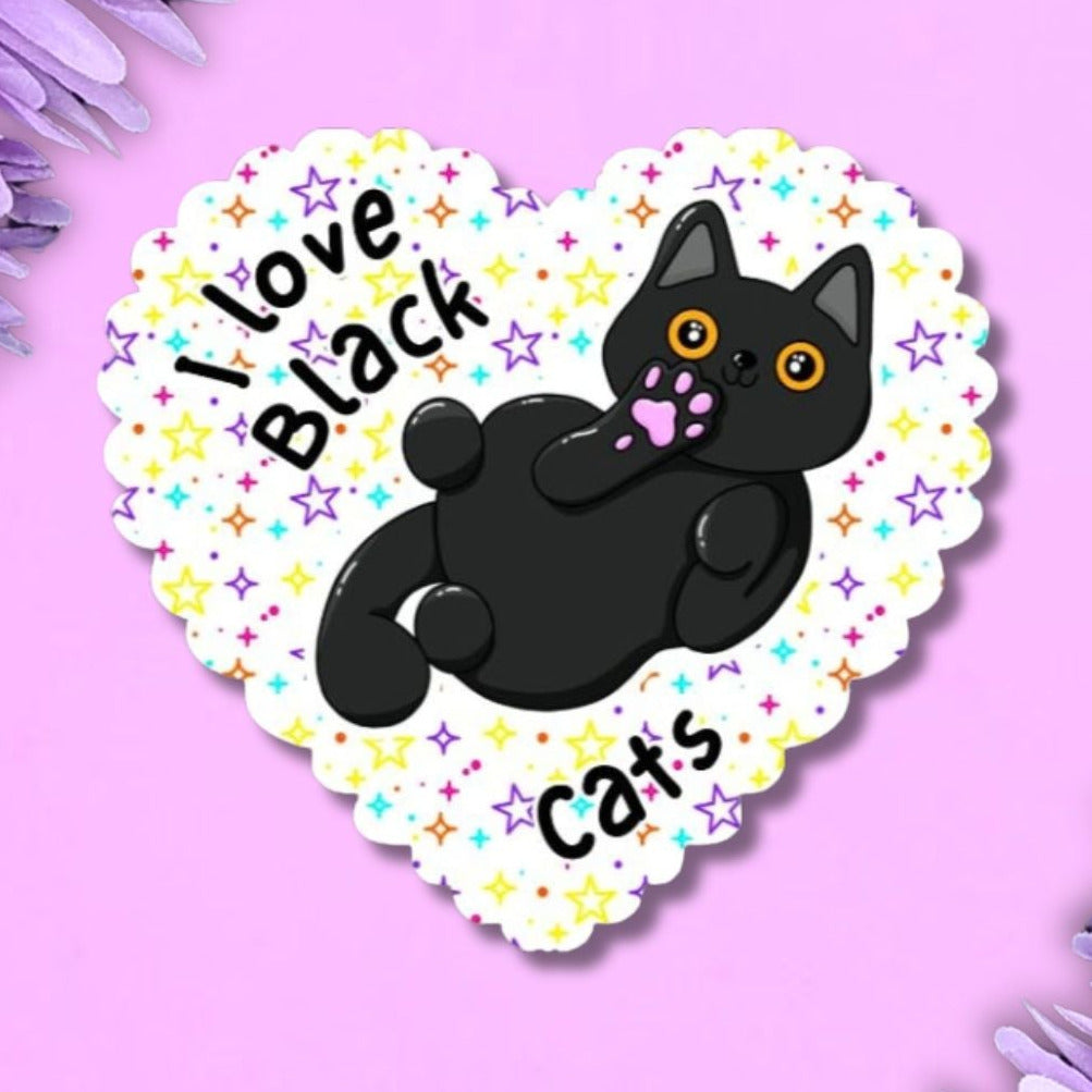 A heart-shaped sticker featuring a black cat illustration and the text 'I love Black cats' on a pastel multicolor star-patterned background, displayed on a purple background with purple flowers in the corners.