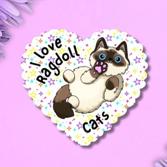 A heart-shaped sticker featuring an illustration of a ragdoll cat, with the text 'I love Ragdoll Cats' on a white scalloped border with small colourful stars. The sticker is displayed on a light purple background framed by purple flowers in the corners.