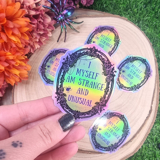 Holo sticker of an oval shaped mirror with gothic decorative frame and text in the mirror saying "I myself am strange and unusual"