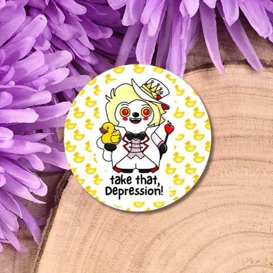 A round pin badge featuring a cartoon character with the text 'take that, Depression!' and a yellow duck motif, displayed on a wooden surface with purple flowers.