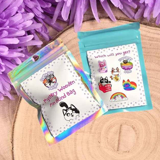 Two small mystery pin packs placed on a round wood slice, with purple flowers around the top edge and green grass underneath. 