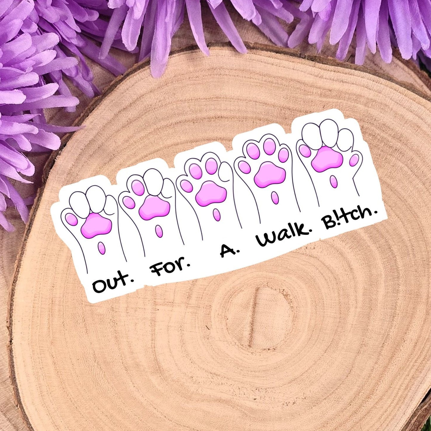 Sticker with paw prints and text on a wooden surface with purple flowers in the background