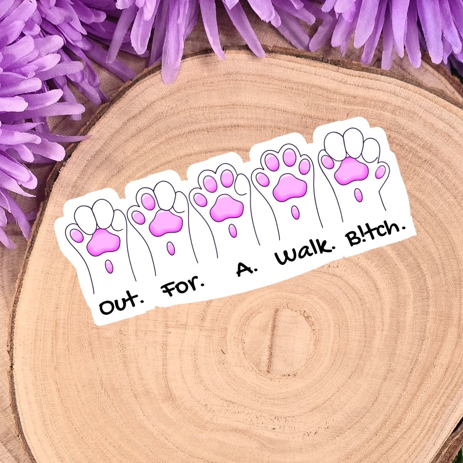 Sticker with paw prints and text on a wooden surface with purple flowers in the background