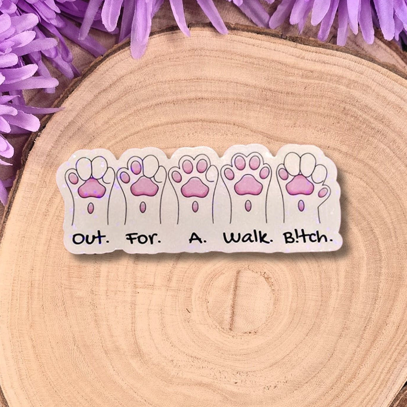 out. for. a . walk .bitch. with white cat paws sticker. sticker ontop of a piece of wood with purple flowers around the top