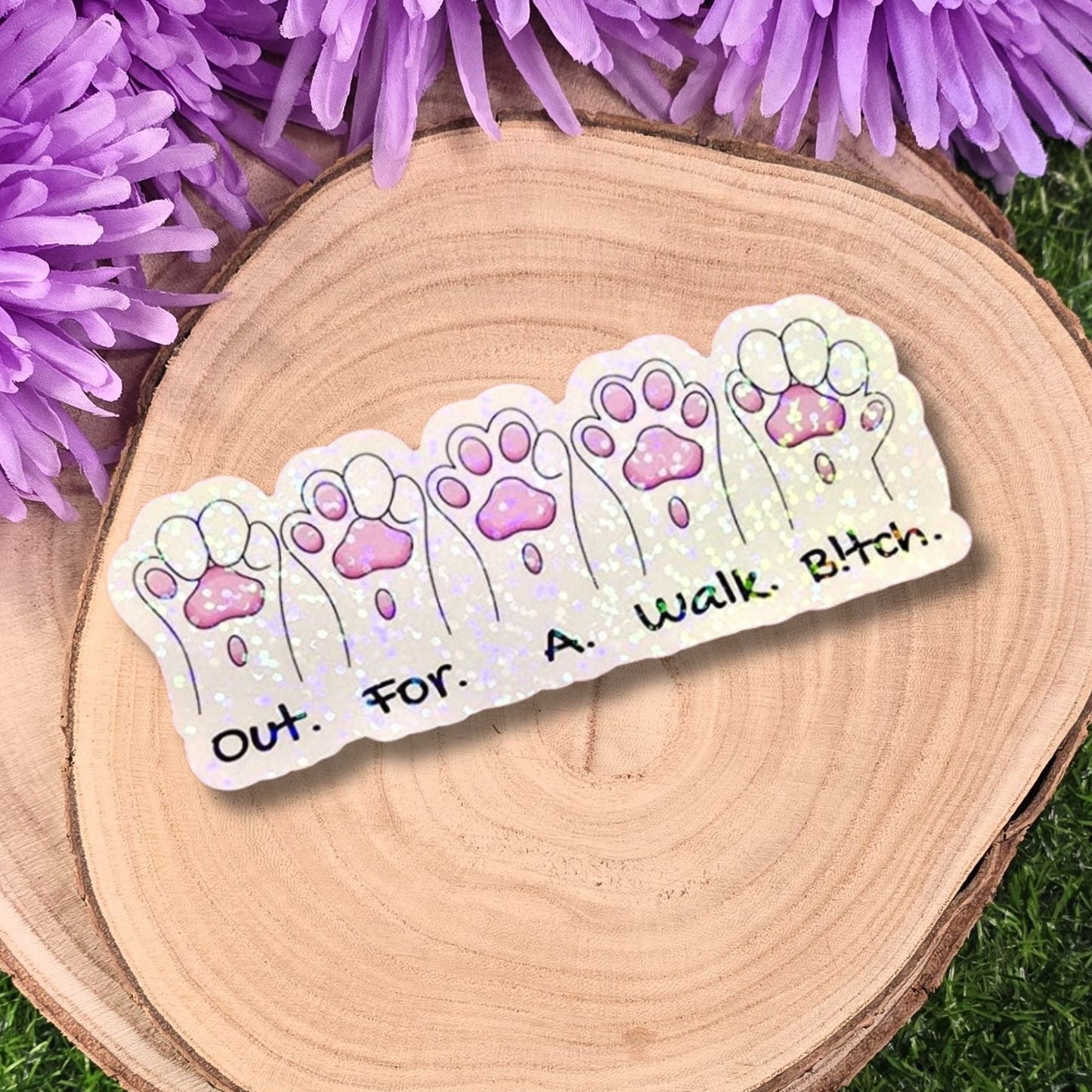 Sticker with paw prints and text on a wooden surface with purple flowers