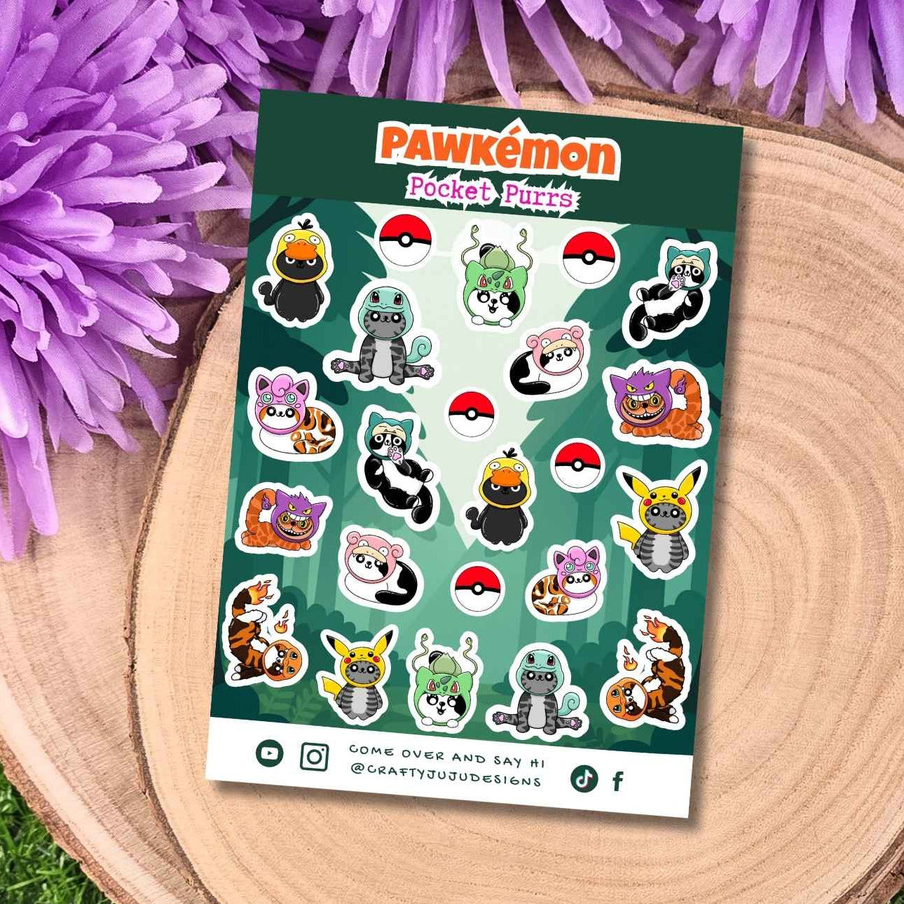A sheet of Pawkmón stickers featuring various cute Pokémon characters and red-and-white Pokéball icons, placed on a round wooden slice with purple flowers and green grass around it.