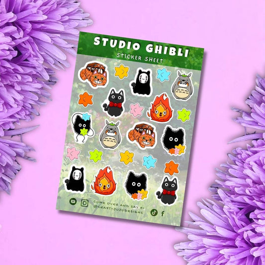 A sticker sheet featuring characters from Studio Ghibli's animated films, displayed diagonally on a pink background with purple flowers framing the edges. The sticker sheet has a green header with 'STUDIO GHIBLI STICKER SHEET' in white text, and contains various cute illustrations of Totoro, No-Face, Catbus, Flamingo, and other characters.
